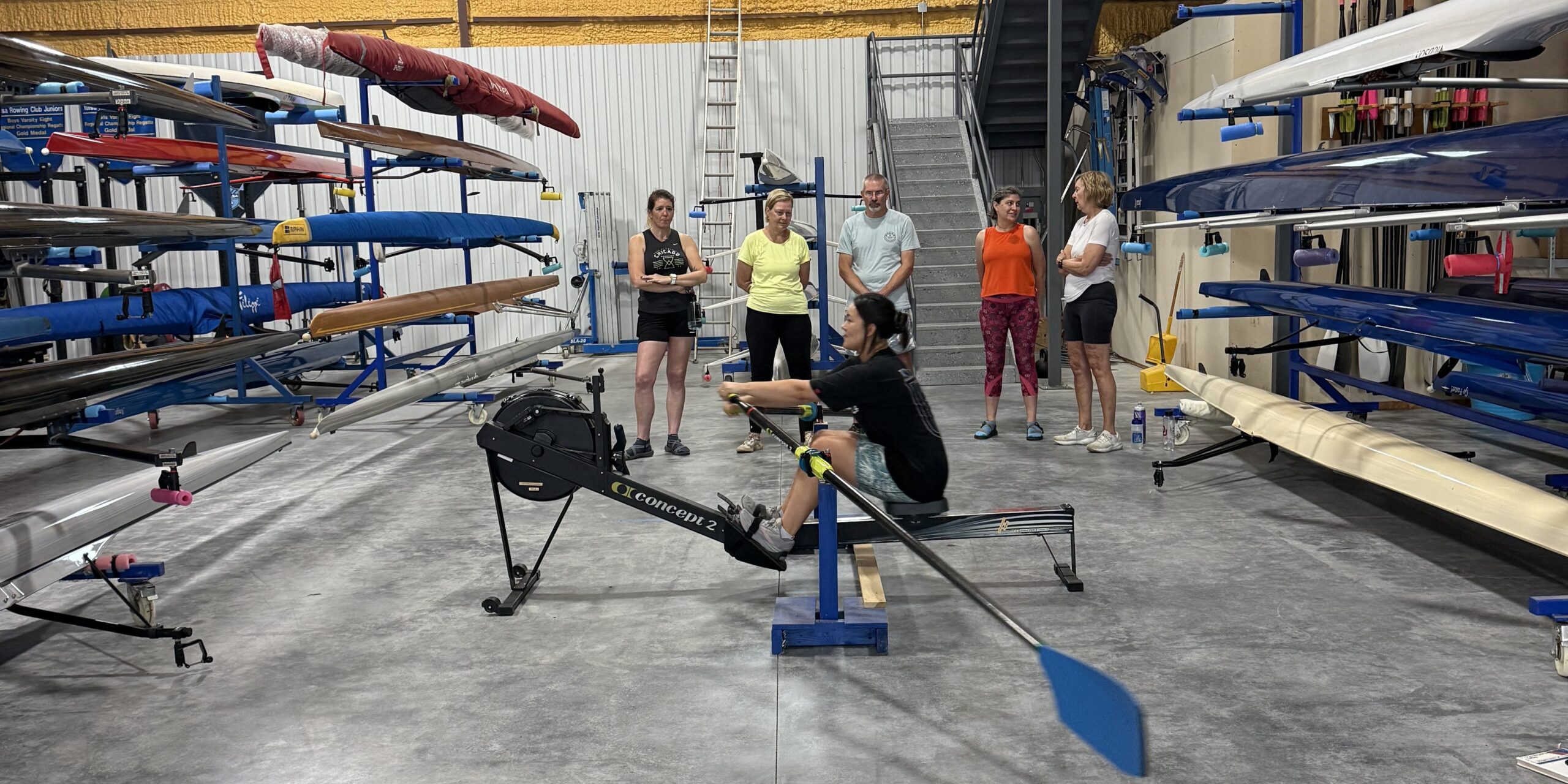 Rowing lesson inside the Tulsa Rowing Club boathouse, with a rower practicing on an indoor rowing machine